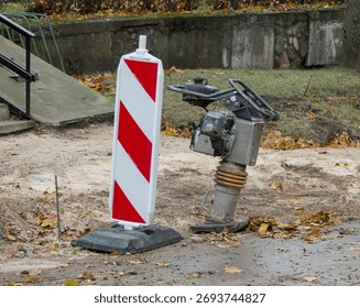 A vibratory plate compactor machine for soil and asphalt at a construction site next to a safety barrier