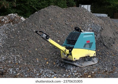 Vibratory plate compactor on a construction site next to a pile of gray gravel.