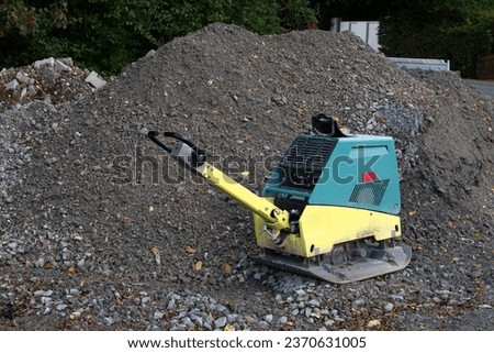 Vibratory plate compactor on a construction site next to a pile of gray gravel.
