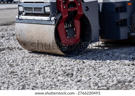 Vibratory roller drum and side frame working over coarse gravel surface, road building equipment for ground compaction and site leveling