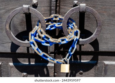 Vicenza, Venetien - Italy - 06-12-2021: Rusty iron rings hold a blue painted chain secured by a gold padlock on an old wooden gate, combining old and modern - Powered by Shutterstock