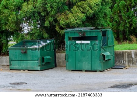 In the vicinity of an apartment building, there is a container bin for garbage