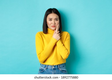 Victim Of Domestic Violance, Young Asian Woman, Touching Cheek And Frowning, Being Slapped In Face, Standing Over Blue Background