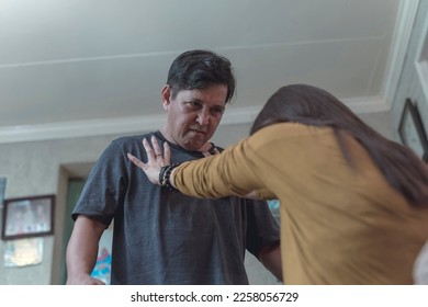 A victimized woman tries to push away her angry and unhinged husband. Example of conflict and physical abuse in intimate relationships. - Shutterstock ID 2258056729