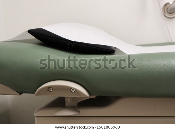 victoria, BC /
Canada - Dec 02 2019: doctors office examination table with fresh
white paper, black pillow, and green mattress.  Clean and ready for
use.  Showing top/head of
bed.