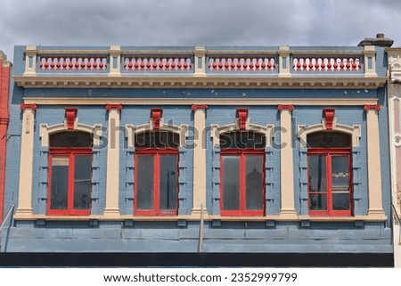 Victorian commercial terrace facade upper floor painted blue-red-cream with balustrade parapet, and cantilevered awning over the footpath frontshops of Sturt Street south side. Ballarat-VIC-Australia.
