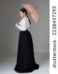 A Victorian or Edwardian woman wearing a garibaldi blouse and black skirt and holding a vintage parasol