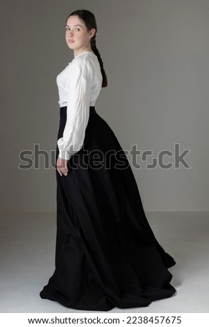 A Victorian or Edwardian woman wearing a white linen Garibaldi blouse and black skirt against a studio backdrop 