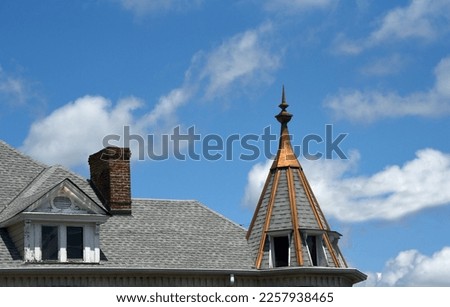 Victorian home grey shingles with turret.  Turret is trimmed in copper with filial.  Windows are constructed around turret top.