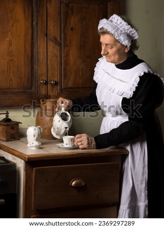 Victorian maid or servant in black dress, lace cap and white apron working in a 19th century interior