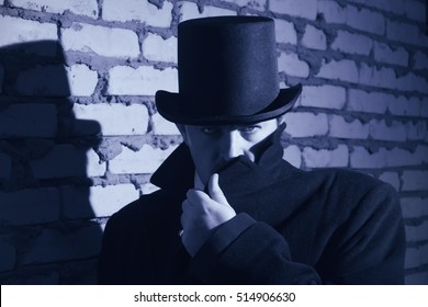 Victorian man in the black coat, top hat and in a tie on a wall background