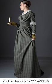 A Victorian Woman Wearing A Dark Green Checked Bodice And Skirt And Holding A Candle