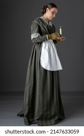 A Victorian Woman Wearing A Dark Green Checked Bodice And Skirt And Holding A Candle