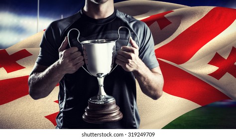 Victorious rugby player holding trophy against rugby stadium - Powered by Shutterstock