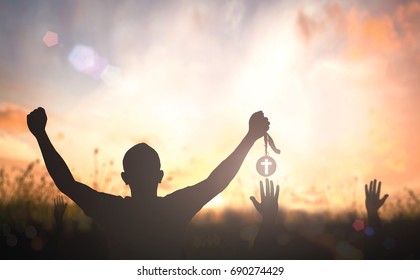 Victory concept: Silhouette christian hand holding medal of cross against blurred meadow autumn sunrise background. - Shutterstock ID 690274429