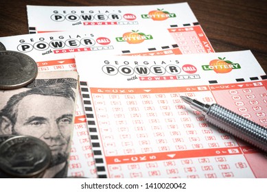 Vidalia, Georgia/ USA - May 27, 2019: A Spread Of Georgia Lottery's Official Blank Numbers Sheet For The Wildly Popular Powerball Lotto Set On Dark Wood Table Background With US Currency And A Pen.