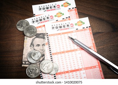 Vidalia, Georgia/ USA - May 27, 2019: A Spread Of Georgia Lottery's Official Blank Numbers Sheet For The Wildly Popular Powerball Lotto Set On Dark Wood Table Background With US Currency And A Pen.