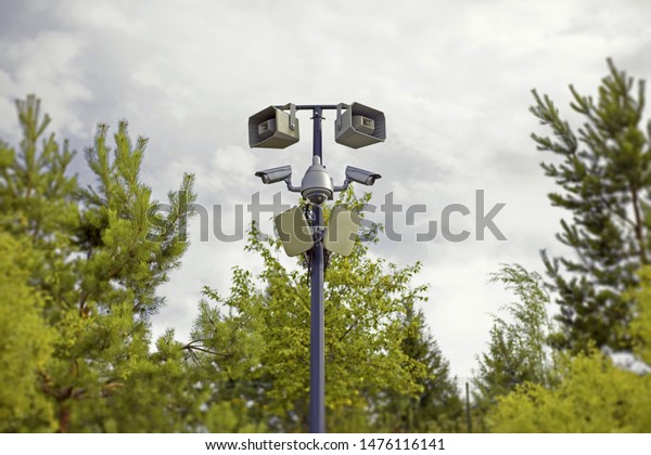 video and audio\
surveillance system on a pole in the city park among the trees, big\
brother is watching us