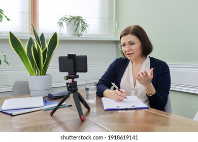Video blog vlog help of professional psychologist. Mature confident woman counselor recording video stream, online consultation group and individual, female using smartphone on tripod for video chat