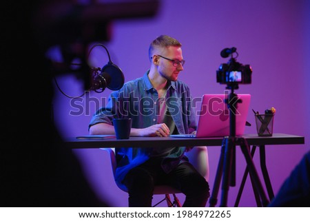 A video blogger records content in his studio. The backstage photo was taken from behind one of the participants in the shooting, at the beginning of the shooting when the blogger is preparing for the