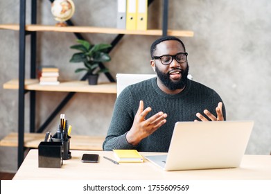 Video call. Attractive African-American guy is using laptop for video communication, a guy in glasses sits at the table in modern office, looking into webcam and talking online - Shutterstock ID 1755609569