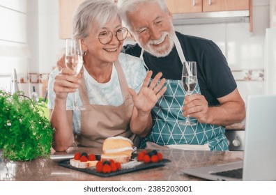 Video call concept. Cheerful senior couple in home kitchen holding drinking glass talking on laptop using computer webcam to communicate in video chat. - Powered by Shutterstock