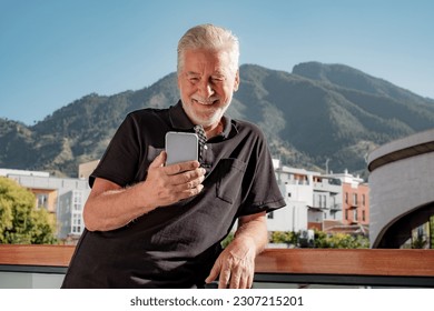 Video Call Concept. Smiling Bearded Senior Man Relaxing  Outdoor Using Mobile Phone. Mountain Landscape in Background - Powered by Shutterstock