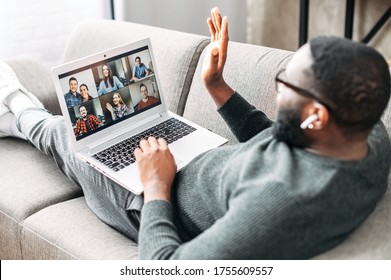 Video Call Concept, Virtual Meeting. Young African-American Guy Relaxed Lays On The Couch And Is Talking Online Via Video Call With Group Of Friends Or Employees.