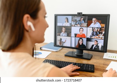 Video Call, Video Meeting. A Young Woman Connect With A Many Employees Together Via Video, She Sits At Office Space And Looks At Webcam, Rear View