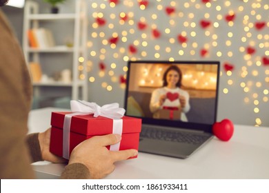 Video call on Saint Valentine's Day. Couple sending each other love and showing presents on virtual date. Closeup of man's hands holding gift box. Shimmering yellow lights, soft focus, selective focus - Powered by Shutterstock