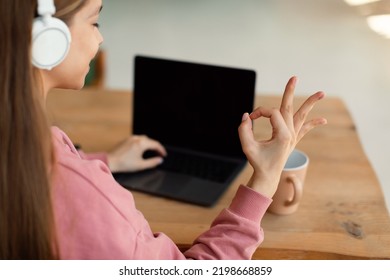 Video Call And Remote Education. Over Shoulder View Of Teen Girl Sitting At Desk And Using Laptop, Showing Ok Gesture. Schoolgirl Having Online Classes. Empty Pc Screen For Mockup