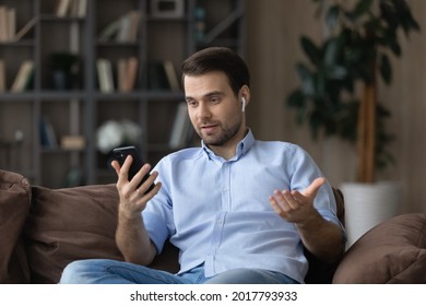 Video calling. Confident male professional specialist sit on couch make answer videocall on cell consult customer from home. Young man expert talk to client give advice consultation use headset phone