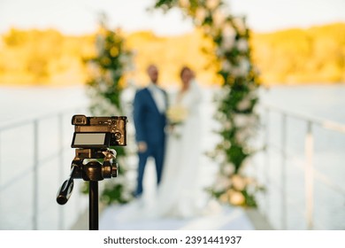 A video camera is filming the bride and groom at the off-site ceremony. Selective focus. Professional videographer and wedding photographer.