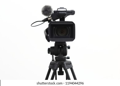 The video camera with the microphone is standing on the tripod isolated on white, in concept of technology, modern, entertainment.