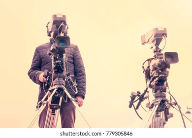 Video camera operator working with his professional equipment in city park, toned