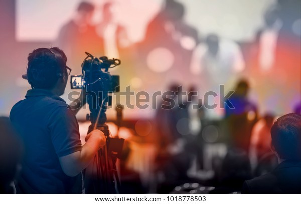 Video camera\
operator working with his equipment at indoor event. Cameraman\
silhouette at meeting\
room\
