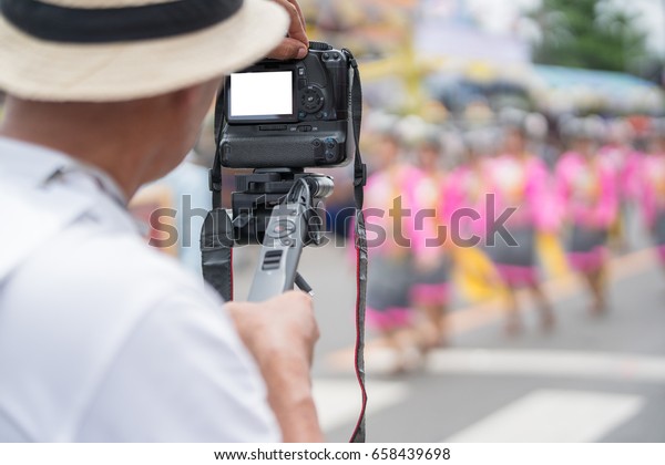Video camera operator working with his\
professional equipment in hand at parade\
festival.