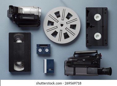 Video Cameras, VHS And Mini Cassettes And A Film Roll Well Arranged Over Blue Background, Above View