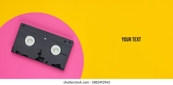 Video Cassette On Yellow Background With Pink Circle And Space For Your Text. Studio Fashion Shot. 80s, Pop Culture. Top View.