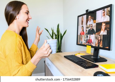 Video Chat, Virtual Morning Meeting. A Young Woman With Cup Of Coffee Is Greeting And Waving To Multiracial Team On The PC Monitor. Side View