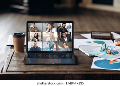 Video conference. Application for remote communication. Screen view of a laptop with people who are communication via video conference. The laptop is on the desktop near a coffee and financial graphs - Shutterstock ID 1748447135