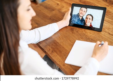 Video Consultation, Video Appointment With Family Psychologist, Doctor. A Woman In White Shirt Is Communicating Via Video With A Couple On The Tablet Screen And Doing Notes In Notebook