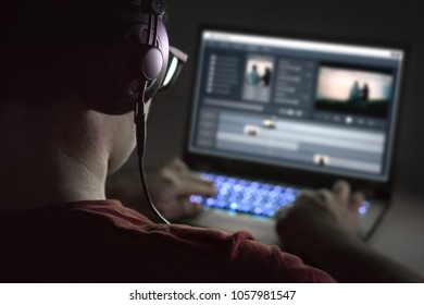 Video editing with laptop. Professional editor adding special effects or color grading footage. Back view of young man using computer software and wearing headphones.
