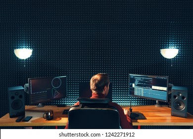 Video editing. Professional editor adding special sound effects. Back view of young man watching graphs on monitors. Copy space on gray wall