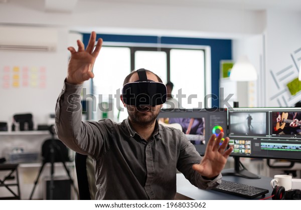 Video editor experiencing virtual reality\
headset, gesturing, editing film montage using post production\
software working in creative agency office. Videographer using VR\
goggles in multimedia\
company