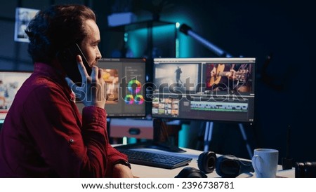 Video editor receiving phone call while arranging recorded stock clips into seamless whole in creative media studio. Videographer talking with director on smartphone while assembling recorded footage