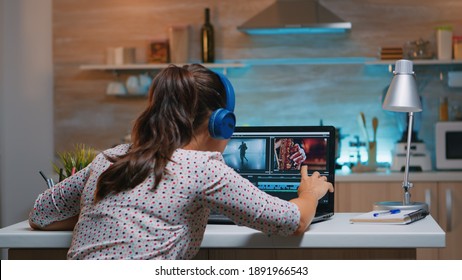 Video Editor Wearing Headset And Working From Home At Digital Project Sitting In The Kitchen. Videographer Editing Audio Film Montage On Professional Laptop Sitting On Desk In Midnight