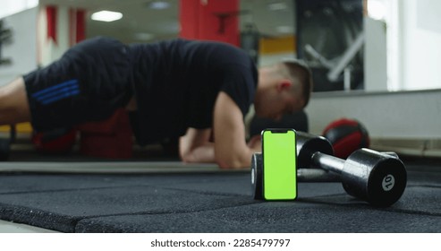 A video featuring a green screen smartphone and a man doing ab exercises in the background. This footage can be used to add customized text, images, or videos to the green screen area - Powered by Shutterstock