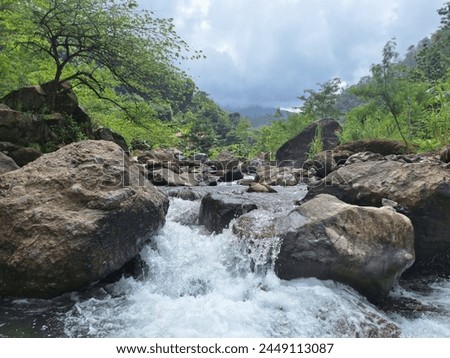 a video footage of a river with lots of rocks and clear water flowing fast. The river is located on the slopes of Mount Muria, Indonesia