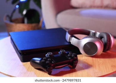 Video game console, wireless controller and headphones on wooden table indoors